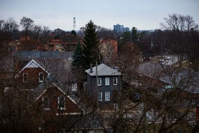 منظر لمدينة برانتفورد الكندية، يظهر منازل تقليدية وأشجار، مع خلفية تضم مباني حديثة، مما يعكس التباين بين التاريخ والحداثة.