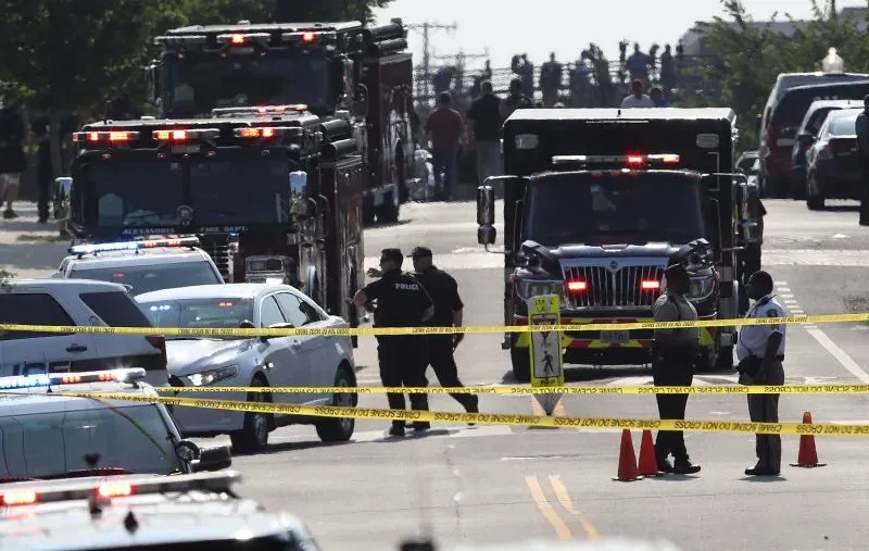 مركبات الطوارئ وعناصر الشرطة في موقع حادث إطلاق نار، مع وجود شريط تحذيري، مما يعكس حالة الطوارئ والتهديدات الأمنية للمشرعين.