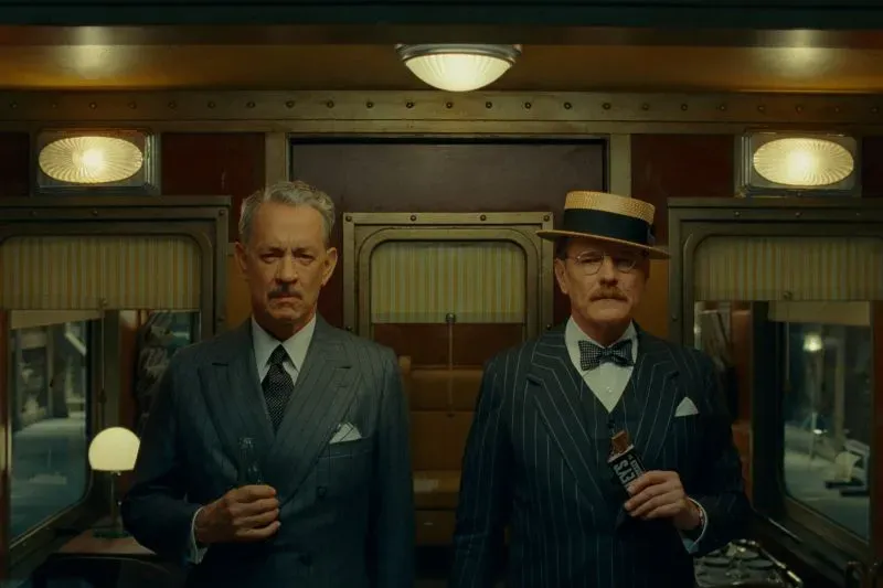 صورة تظهر شخصيتين ترتديان بدلات أنيقة في بيئة داخلية، تعكس أسلوب ويس أندرسون الفريد في تصميم الأزياء في فيلمه "المخطط الفينيقي".