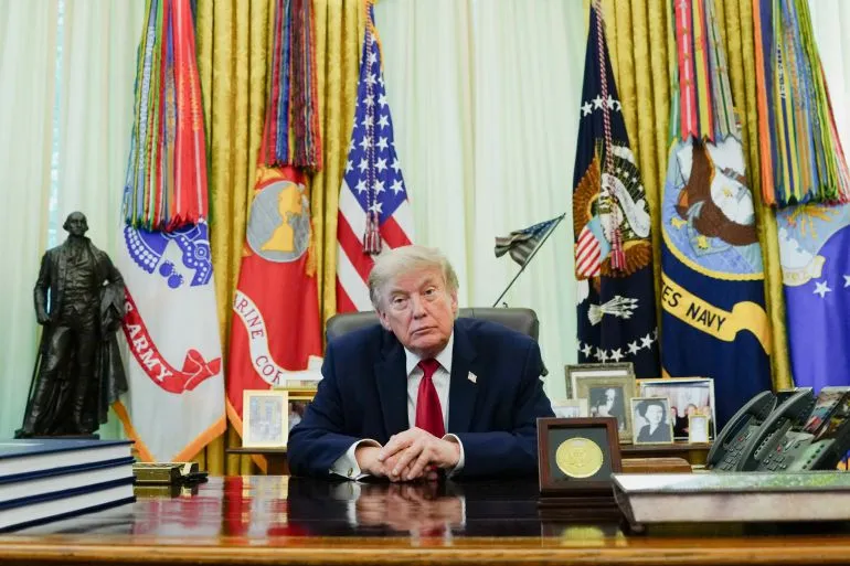 الرئيس الأمريكي دونالد ترامب في المكتب البيضاوي وسط أعلام الجيش الأمريكي، يتأمل الخيارات العسكرية والسياسية تجاه إيران.