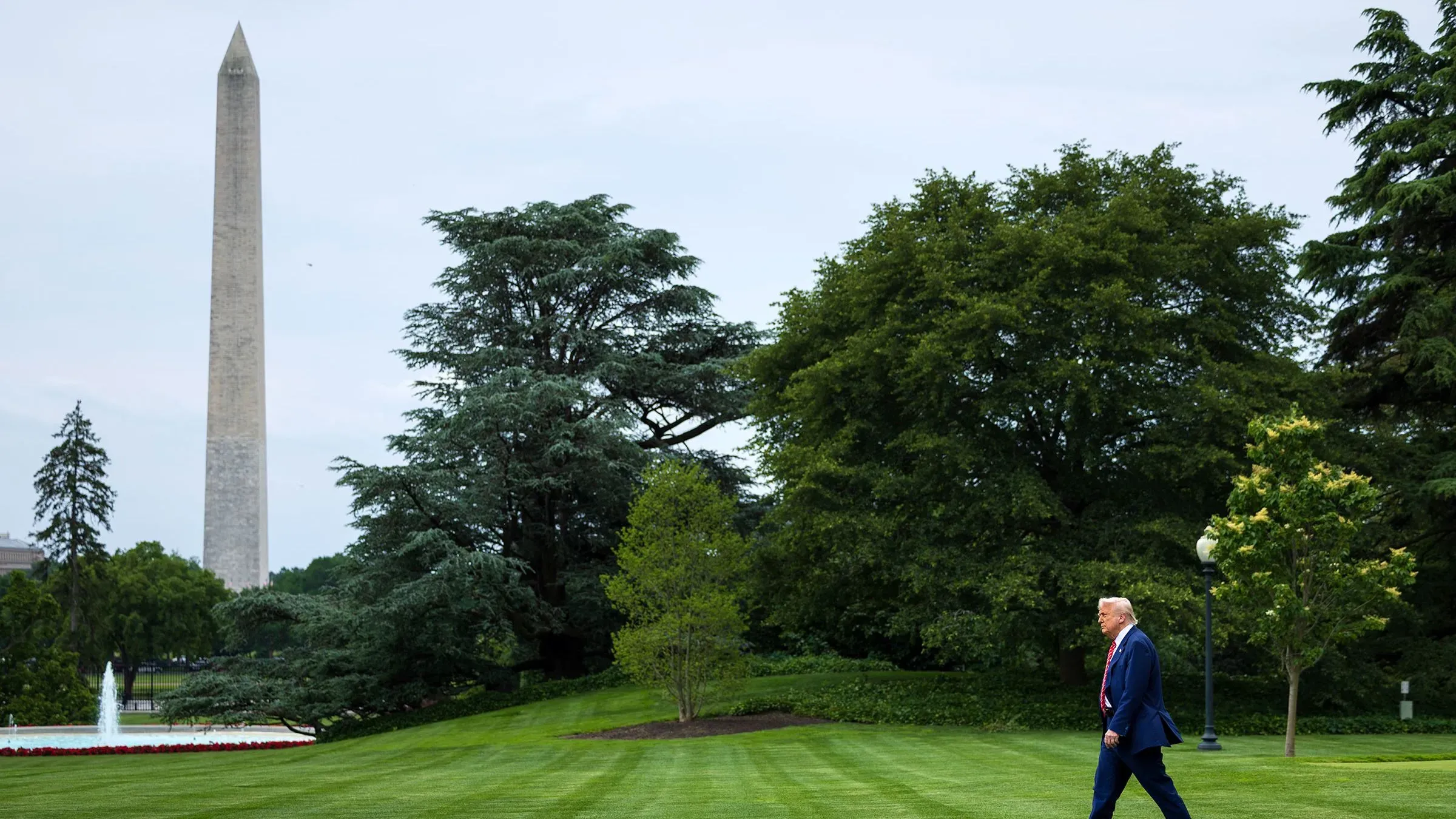 ترامب يسير في حديقة البيت الأبيض، مع نصب واشنطن في الخلفية، مما يعكس التوترات السياسية الحالية في البلاد.