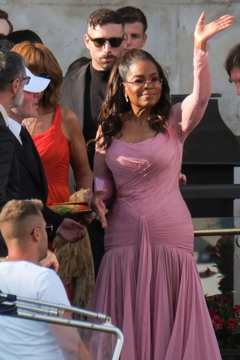 أوبرا وينفري ترتدي فستاناً وردياً وتلوح بيدها أثناء حضورها حفل زفاف جيف بيزوس ولورين سانشيز في جزيرة سان جورجيو ماجيوري.