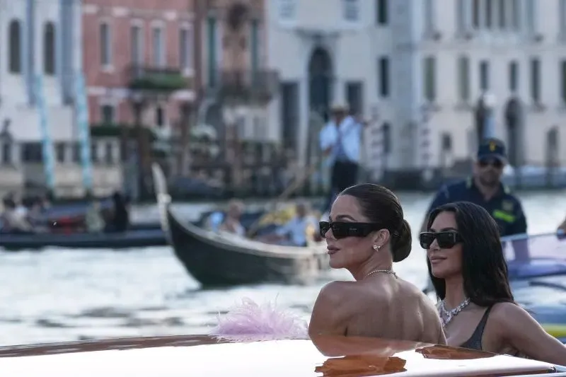امرأتان ترتديان نظارات شمسية، تتجهان نحو حفل زفاف جيف بيزوس ولورين سانشيز في البندقية، مع خلفية من القنوات والمباني التاريخية.