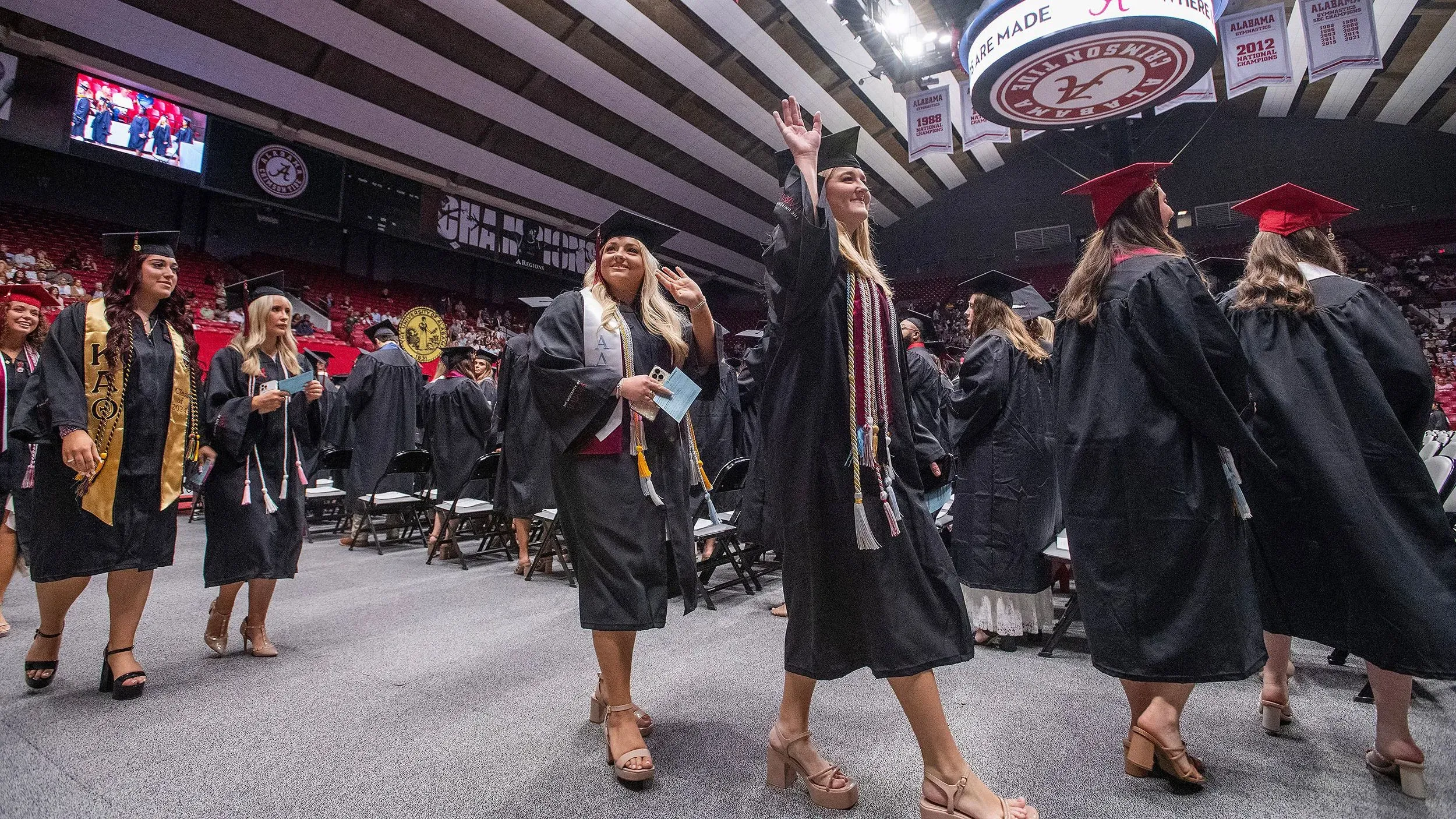 حفل تخرج في جامعة ألاباما، حيث يرتدي الخريجون قبعات وتيجان، مع التركيز على الطلاب أثناء مغادرتهم المنصة.