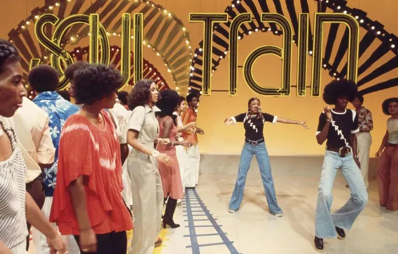 مجموعة من الراقصين في برنامج "Soul Train" يعبرون عن حيوية موسيقى الفانك في السبعينيات، مع خلفية ملونة وأجواء احتفالية.