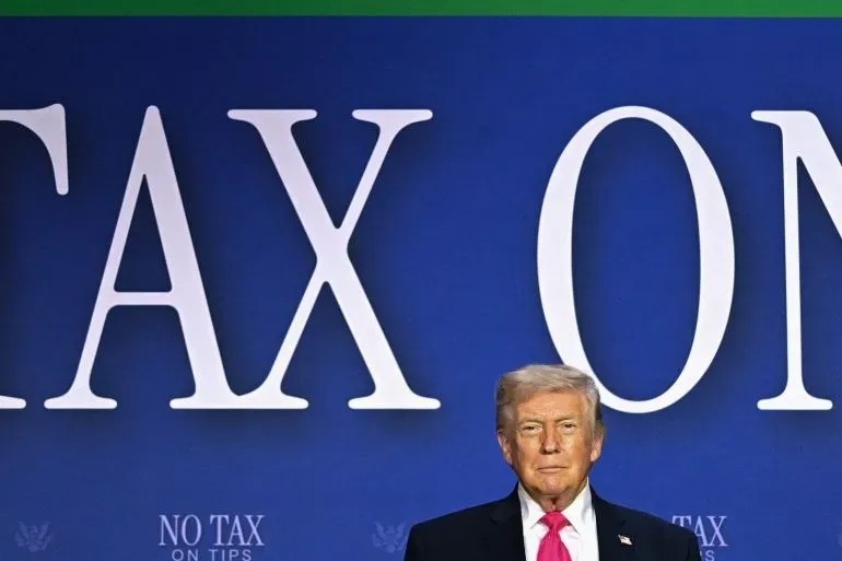 ترامب يقف أمام لافتة كبيرة تتضمن عبارة "لا ضرائب على الإكراميات"، في سياق حديثه عن المفاوضات مع إيران ووقف إطلاق النار.