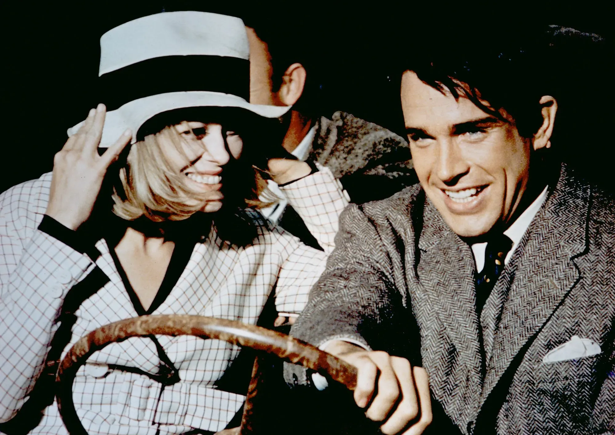 لقطة تظهر شخصين مبتسمين في سيارة، يرتديان ملابس أنيقة تعود لفترة تاريخية سابقة، مما يعكس أجواء الأفلام الكلاسيكية لشركة وارنر بروس.