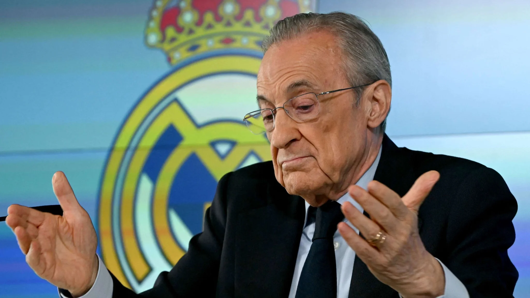 رئيس ريال مدريد فلورنتينو بيريز يعبّر عن رفض صفقة إنزو فيرنانديز وسط خلفية شعار النادي في مؤتمر صحفي.