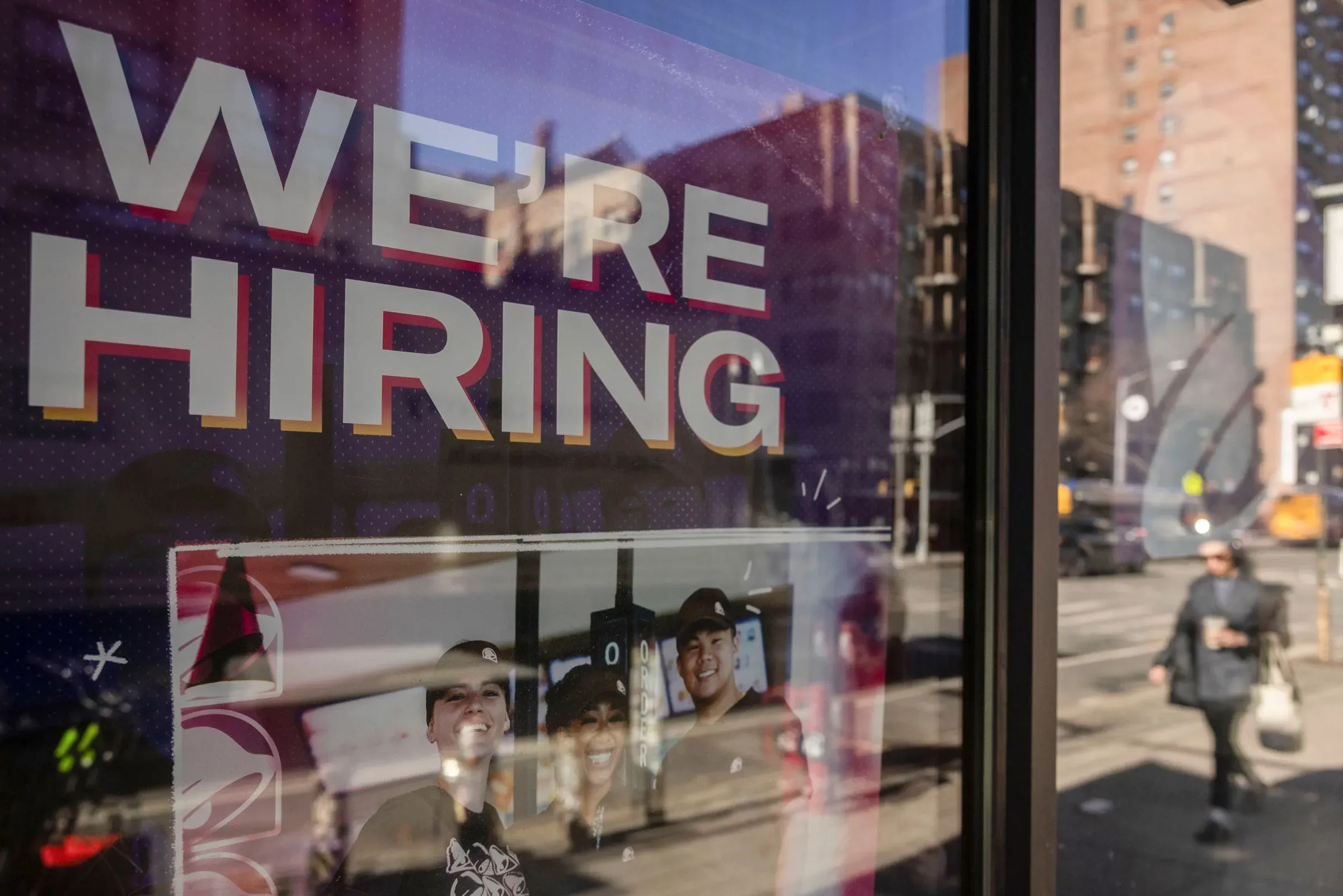 لافتة "نحن نوظف" مع صور لثلاثة موظفين مبتسمين، تعكس حالة سوق العمل في الولايات المتحدة وتوقعات التوظيف لعام 2026.