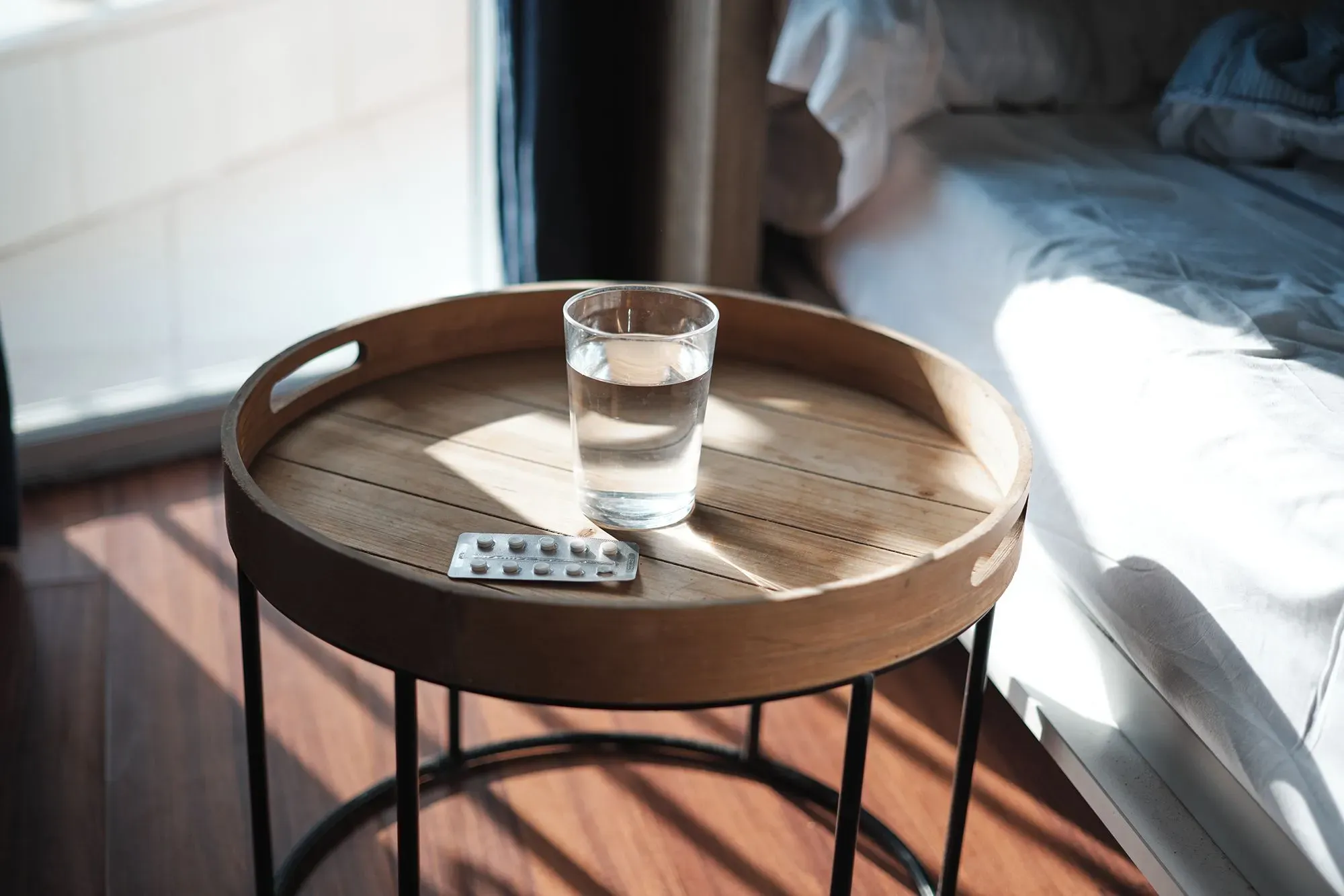 زجاجة ماء وكبسولات الميلاتونين موضوعة على طاولة بجانب السرير، مما يشير إلى استخدام المكملات لتحسين النوم.