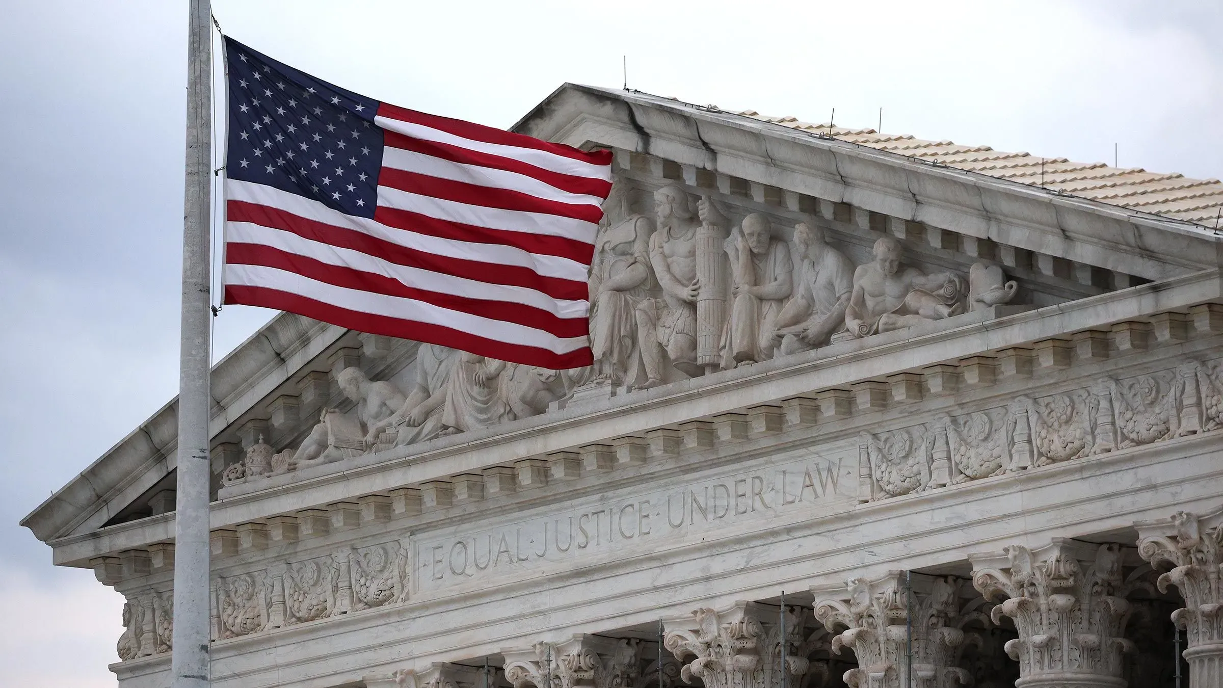 علم أمريكي يرفرف أمام مبنى المحكمة العليا في الولايات المتحدة، مع نقوش تعكس مفهوم العدالة والمساواة.