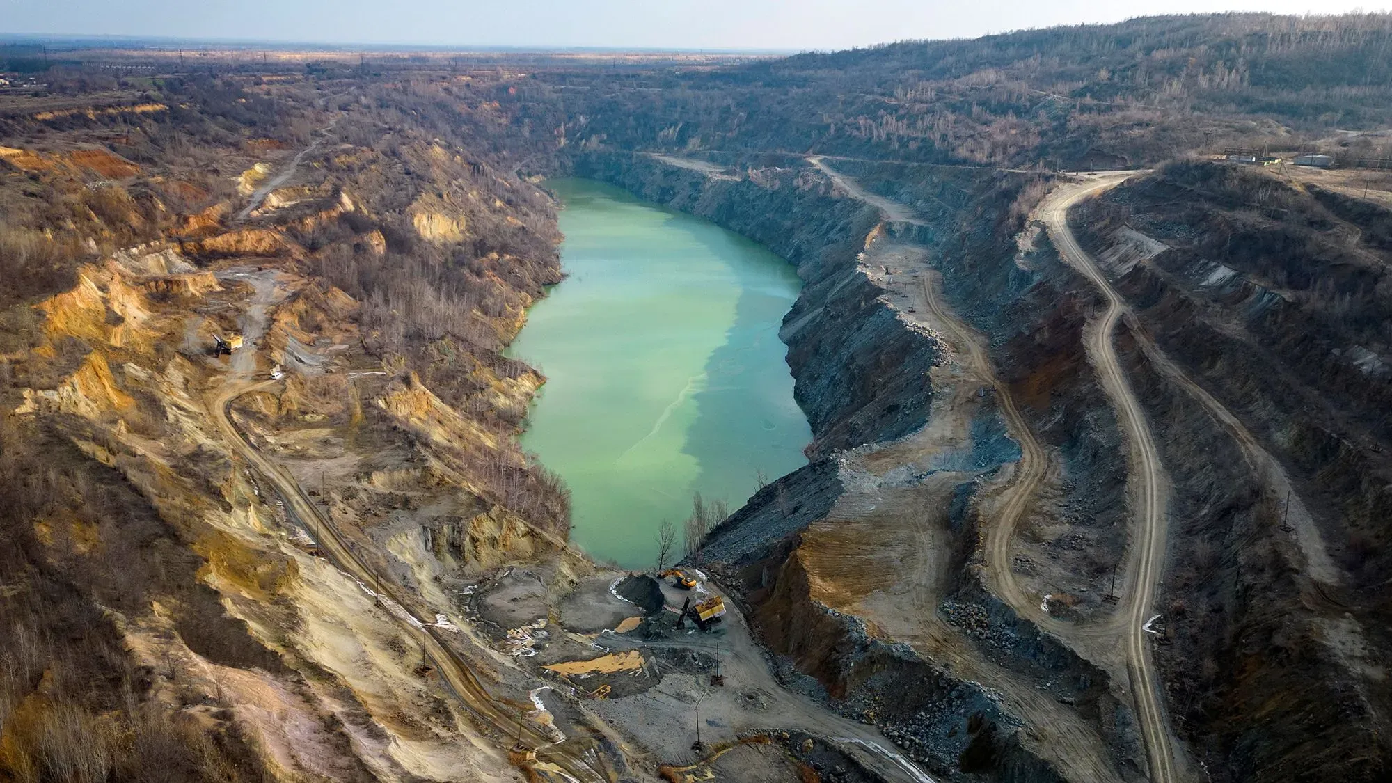 مشهد لعملية استخراج المعادن من محجر، يظهر مياه خضراء وأراضي شبه جافة، يعكس أهمية الموارد الطبيعية في الاتفاق بين الولايات المتحدة وأوكرانيا.