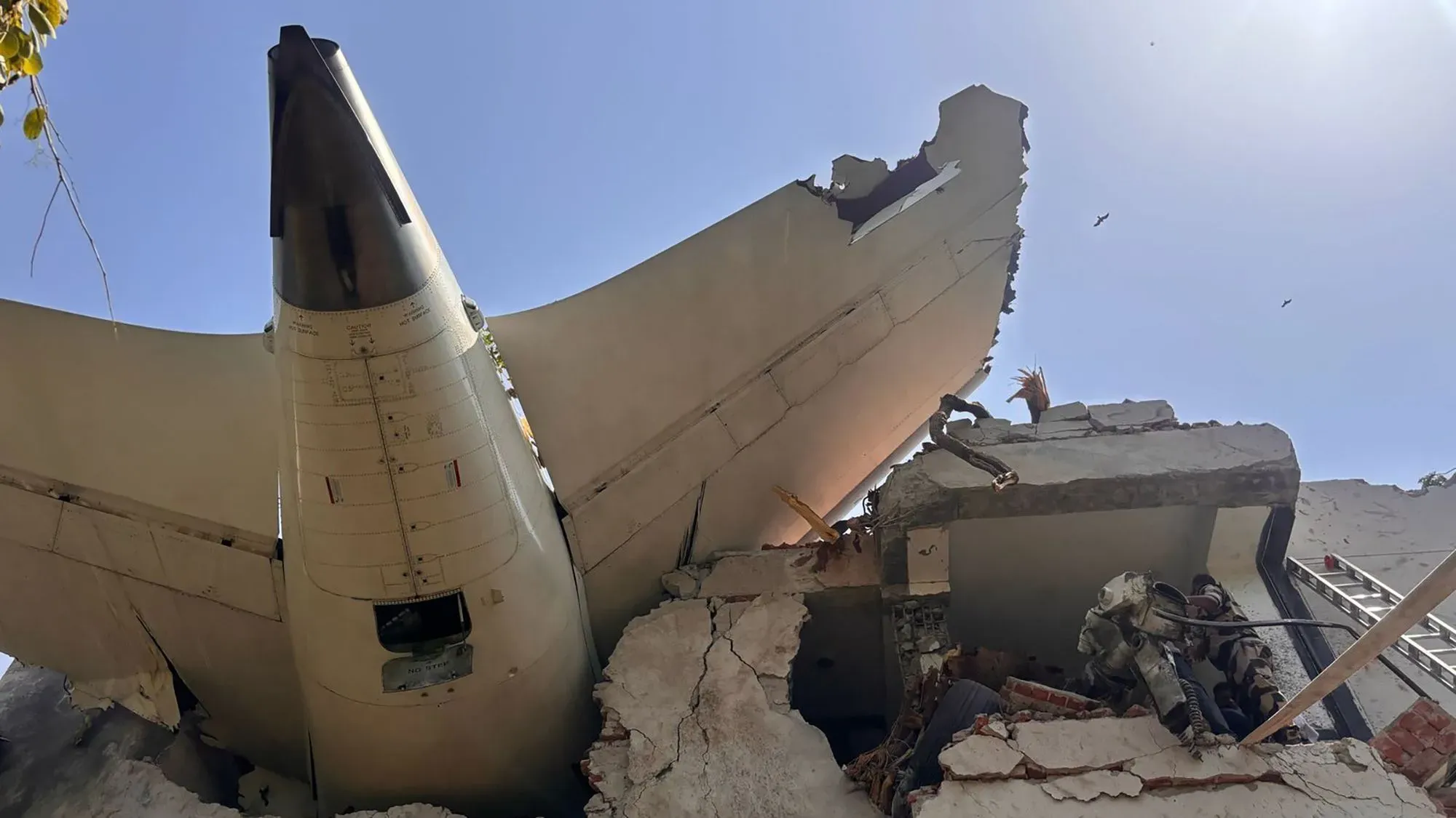 تحطم طائرة بوينج 787-8 دريملاينر تابعة للخطوط الجوية الهندية في أحمد آباد، مع ظهور ذيل الطائرة بارزًا من مبنى مهدوم.