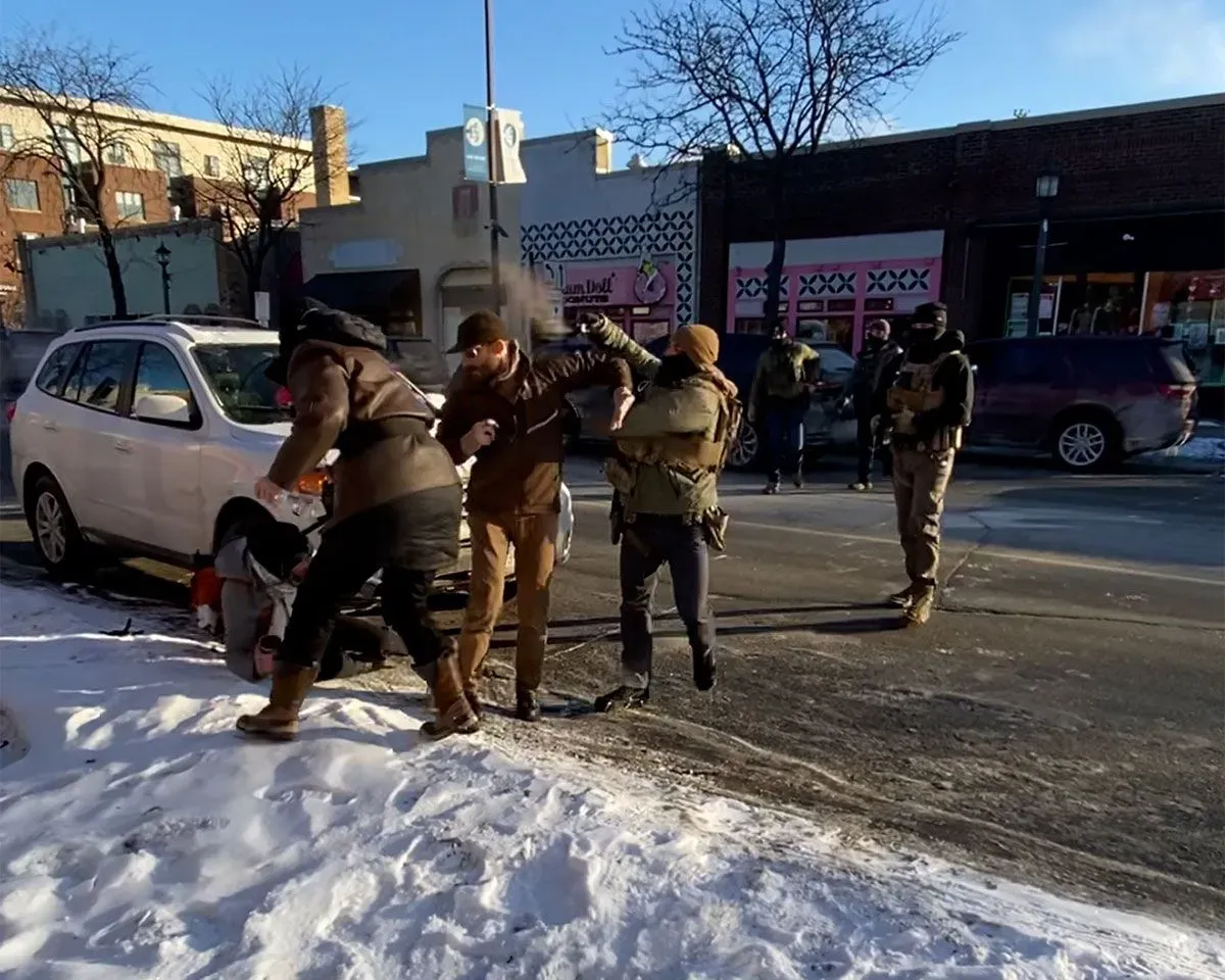 تظهر الصورة لحظة من حادثة إطلاق نار في مينيابوليس، حيث يتصارع ضباط الهجرة مع رجل على الأرض وسط حشود من المتظاهرين.