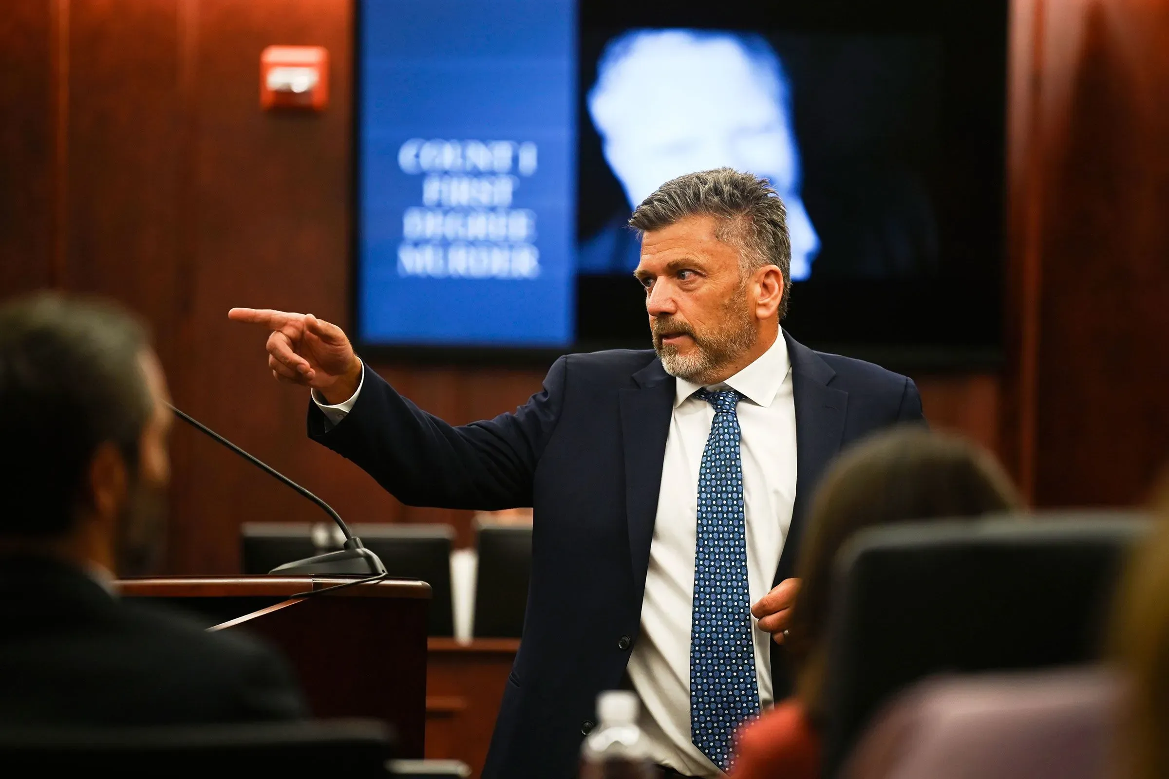 محامي يتحدث في قاعة المحكمة، أثناء محاكمة جيمس كريغ بتهمة القتل، مع شاشة تعرض تفاصيل القضية خلفه.