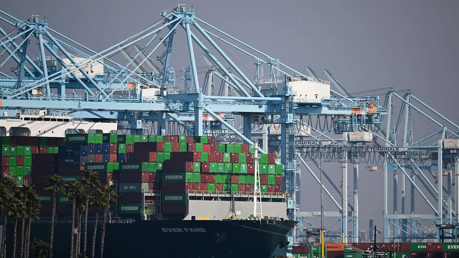 صورة لميناء مزدحم بالحاويات والسفن، حيث تُظهر الرافعات الكبيرة والمعدات المستخدمة في تحميل وتفريغ البضائع، مما يعكس تأثير التعريفات الجمركية على التجارة.