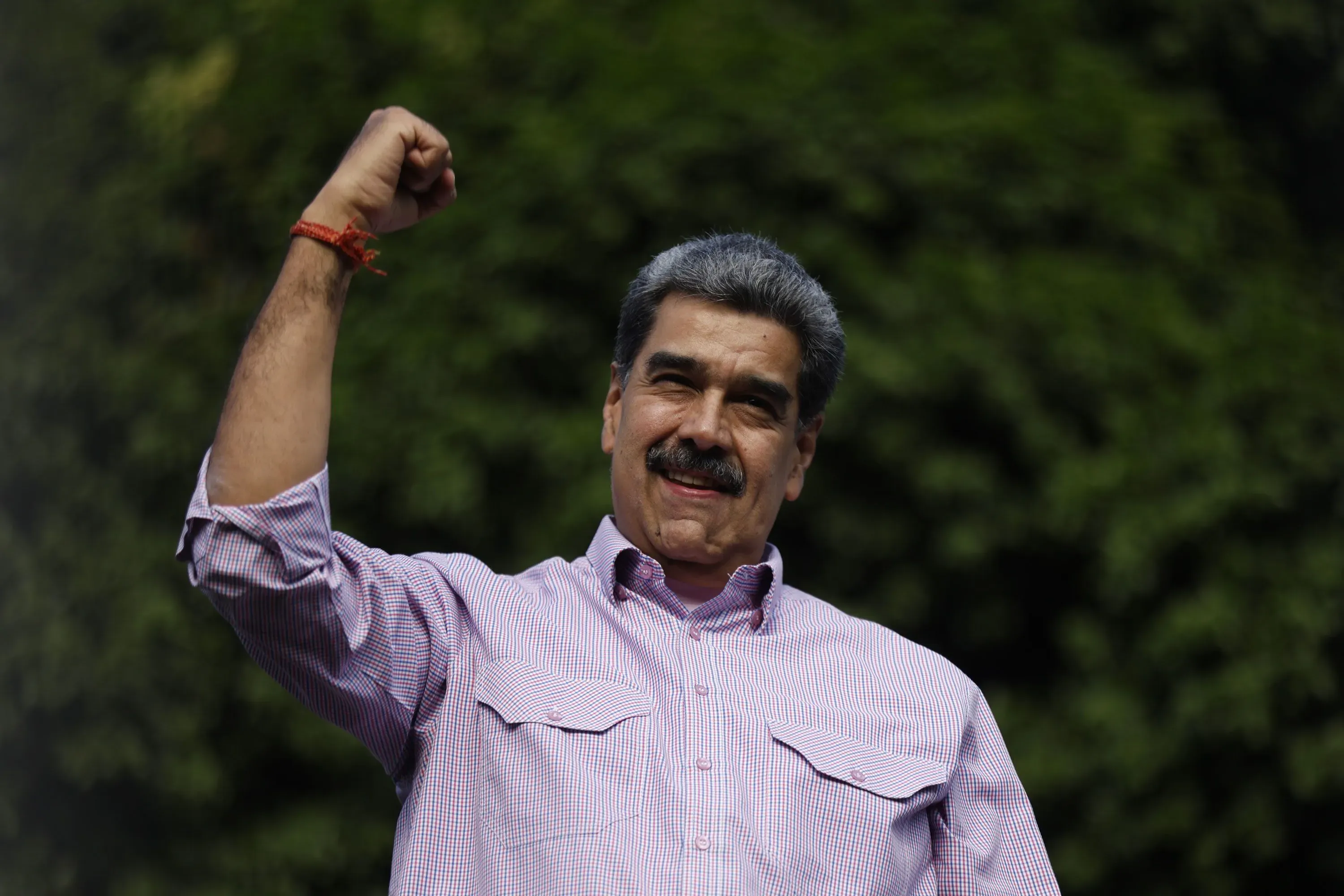 نيكولاس مادورو، رئيس فنزويلا، يرفع يده بإشارة انتصار، وسط خلفية طبيعية، مما يعكس تحدياته السياسية الحالية.