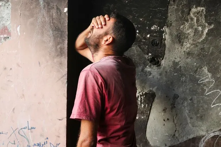 رجل فلسطيني يعبر عن حزنه في مكان متضرر، مما يعكس معاناة السكان في غزة خلال النزاع المستمر.