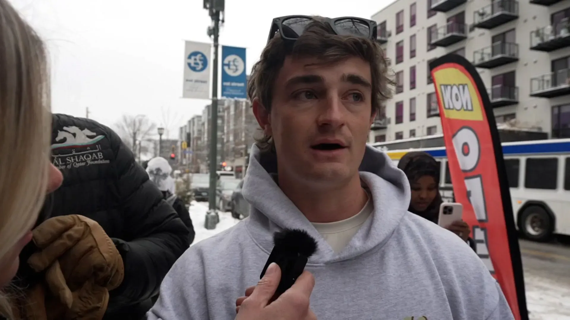 شخص يتحدث في الشارع خلال طقس بارد، محاط بأعلام ولافتات، في سياق جدل حول الاحتيال في مراكز رعاية الأطفال بمينيسوتا.