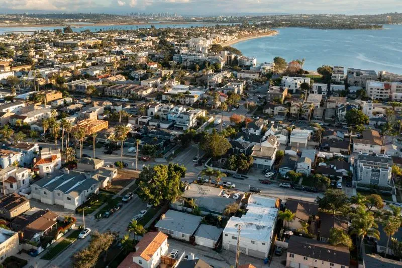 منظر جوي لمدينة ساحلية تضم منازل متعددة الطوابق وشوارع تمتد نحو البحر، مما يعكس ارتفاع أسعار المساكن في الولايات المتحدة.