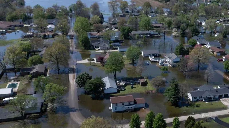 مناطق سكنية غارقة بالمياه بعد الفيضانات، مع منازل وأشجار محاطة بالمياه، تعكس تأثير الكوارث الطبيعية على المجتمعات.