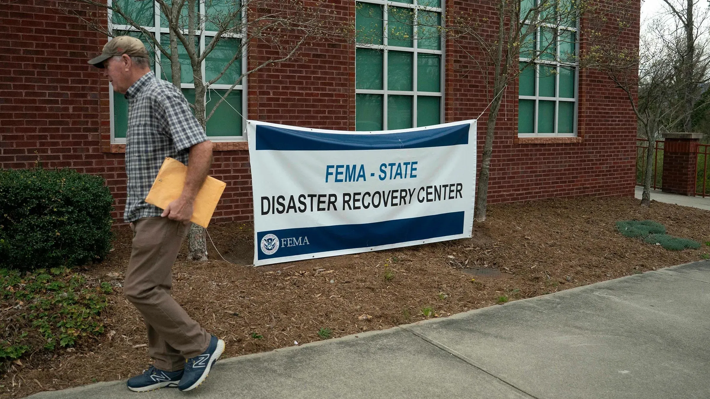 رجل يسير بجوار لافتة مركز استعادة الكوارث التابع للوكالة الفيدرالية لإدارة الطوارئ (FEMA) في ولاية أمريكية، مع التركيز على جهود الإغاثة.