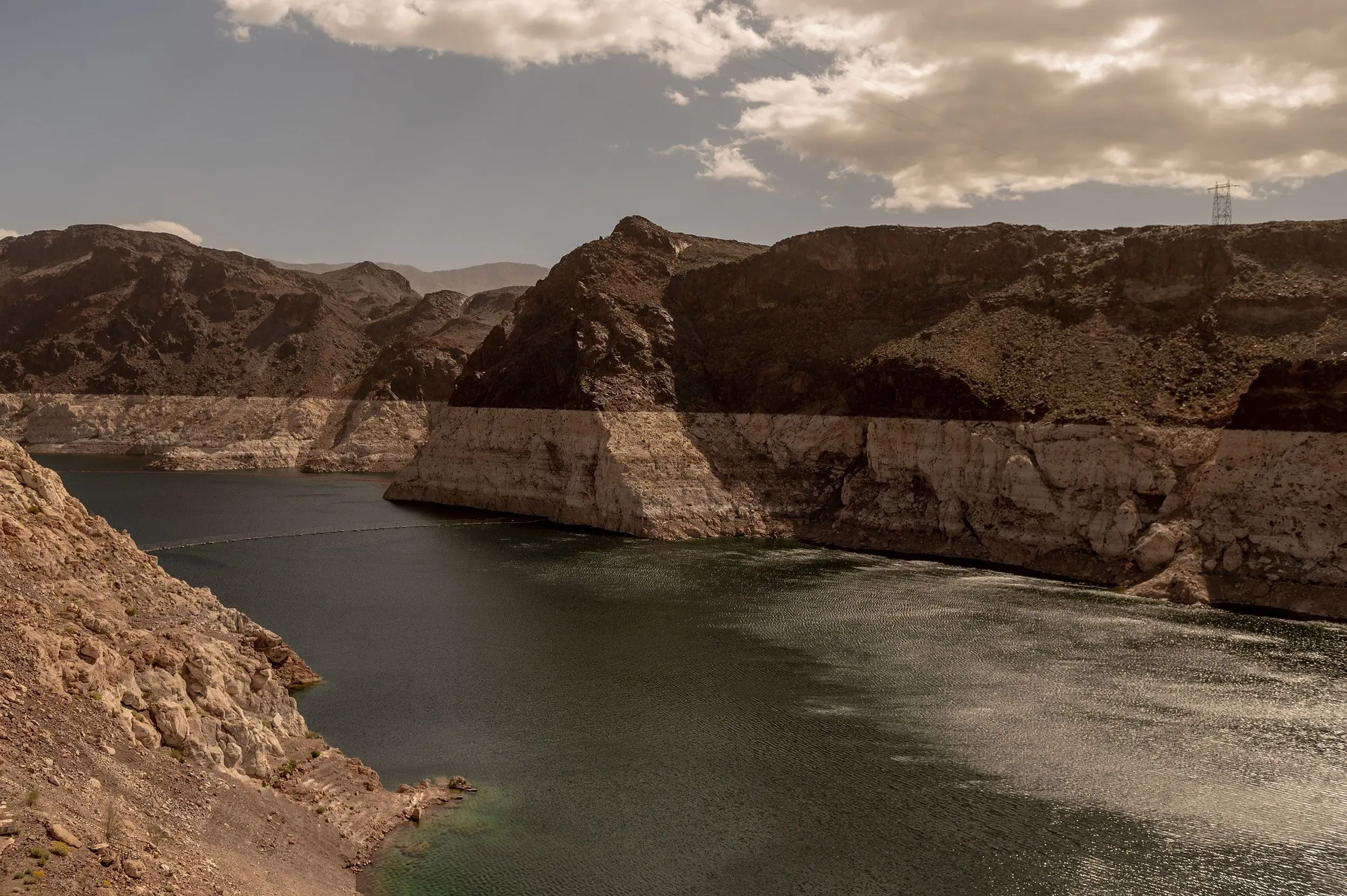 منظر طبيعي يظهر بحيرة ذات مستوى مياه منخفض، محاطة بتضاريس صخرية جافة، مما يعكس تأثيرات الجفاف المتزايد بسبب تغير المناخ.