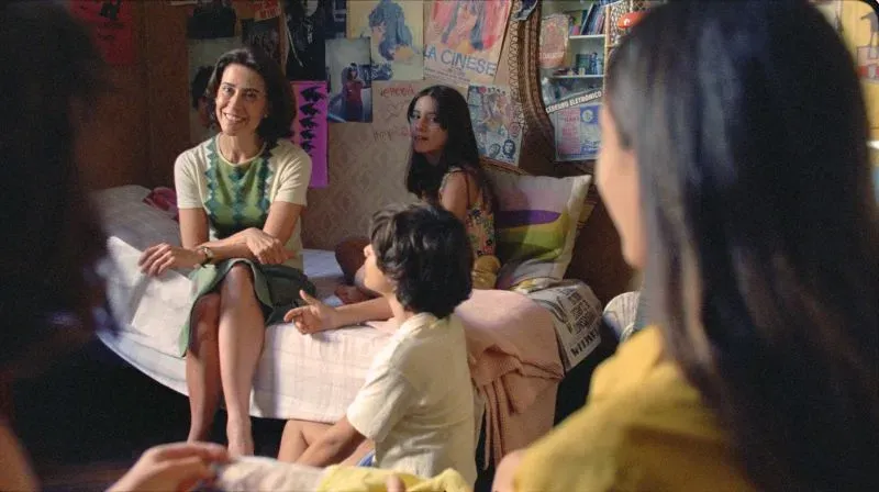 مجموعة من الأشخاص يجلسون في غرفة محاطة باللوحات الفنية، حيث تتوسطهم امرأة تتحدث، مما يعكس جوًا من التفاعل الاجتماعي.