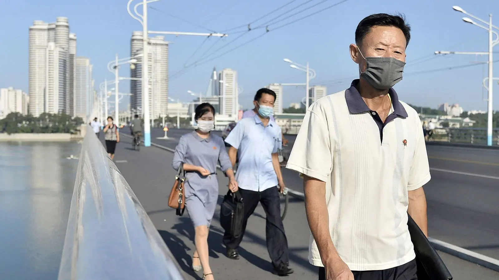 مشاة يرتدون كمامات في شوارع بيونغ يانغ، مع خلفية من المباني الحديثة، تعكس تأثير جائحة كوفيد-19 في كوريا الشمالية.