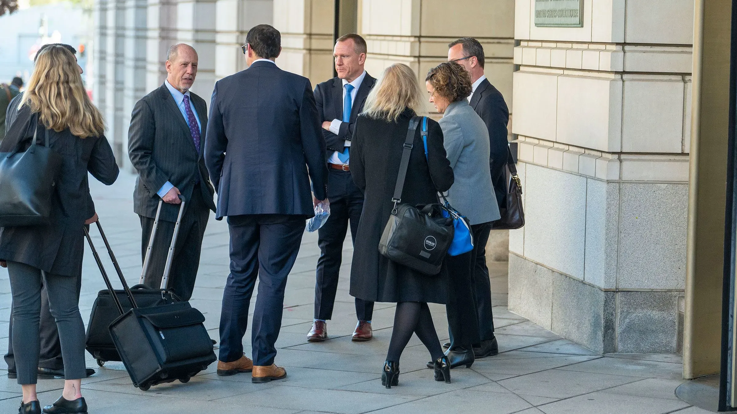 مجموعة من الصحفيين يتجمعون خارج مبنى حكومي، يتبادلون الحديث، مع وجود حقائب سفر بجانبهم، في سياق نقاش حول وصول الإعلام إلى البيت الأبيض.