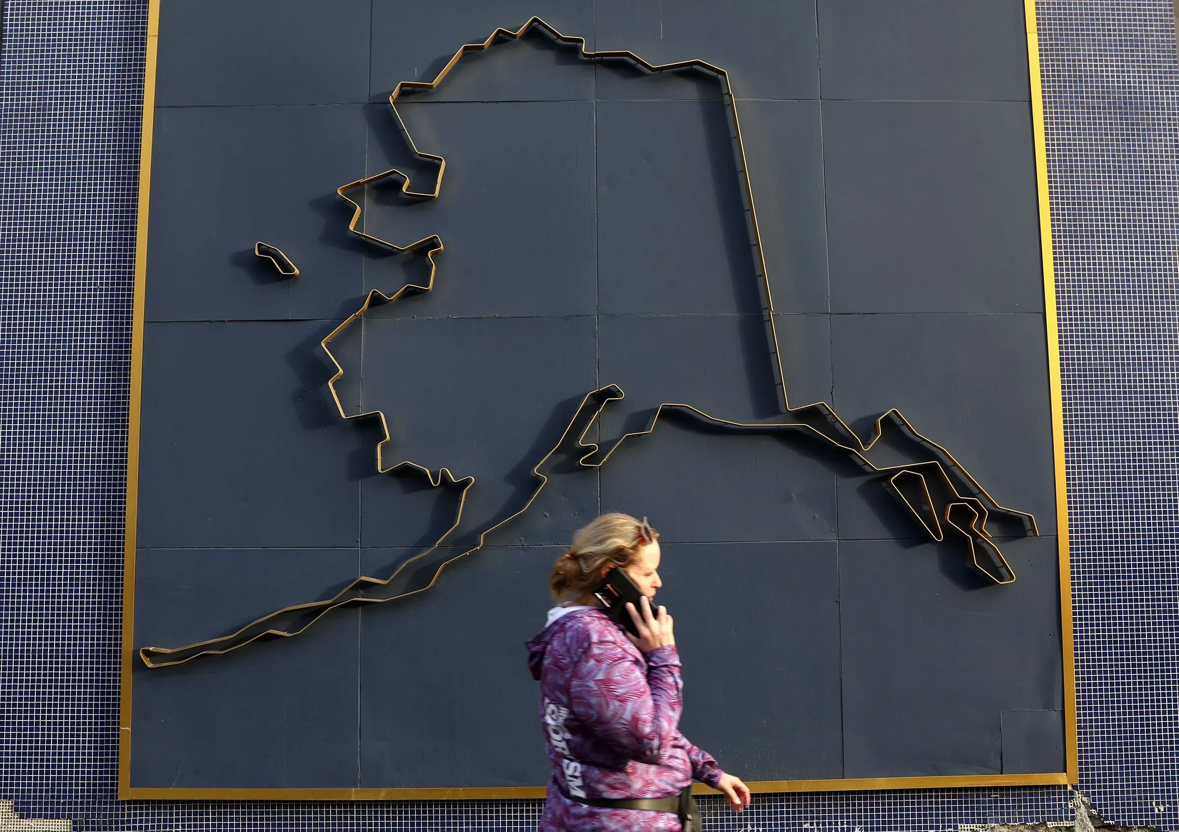 امرأة تتحدث على الهاتف أمام لوحة جدارية توضح خريطة ولاية ألاسكا، في سياق التحضيرات لقمة ترامب وبوتين.