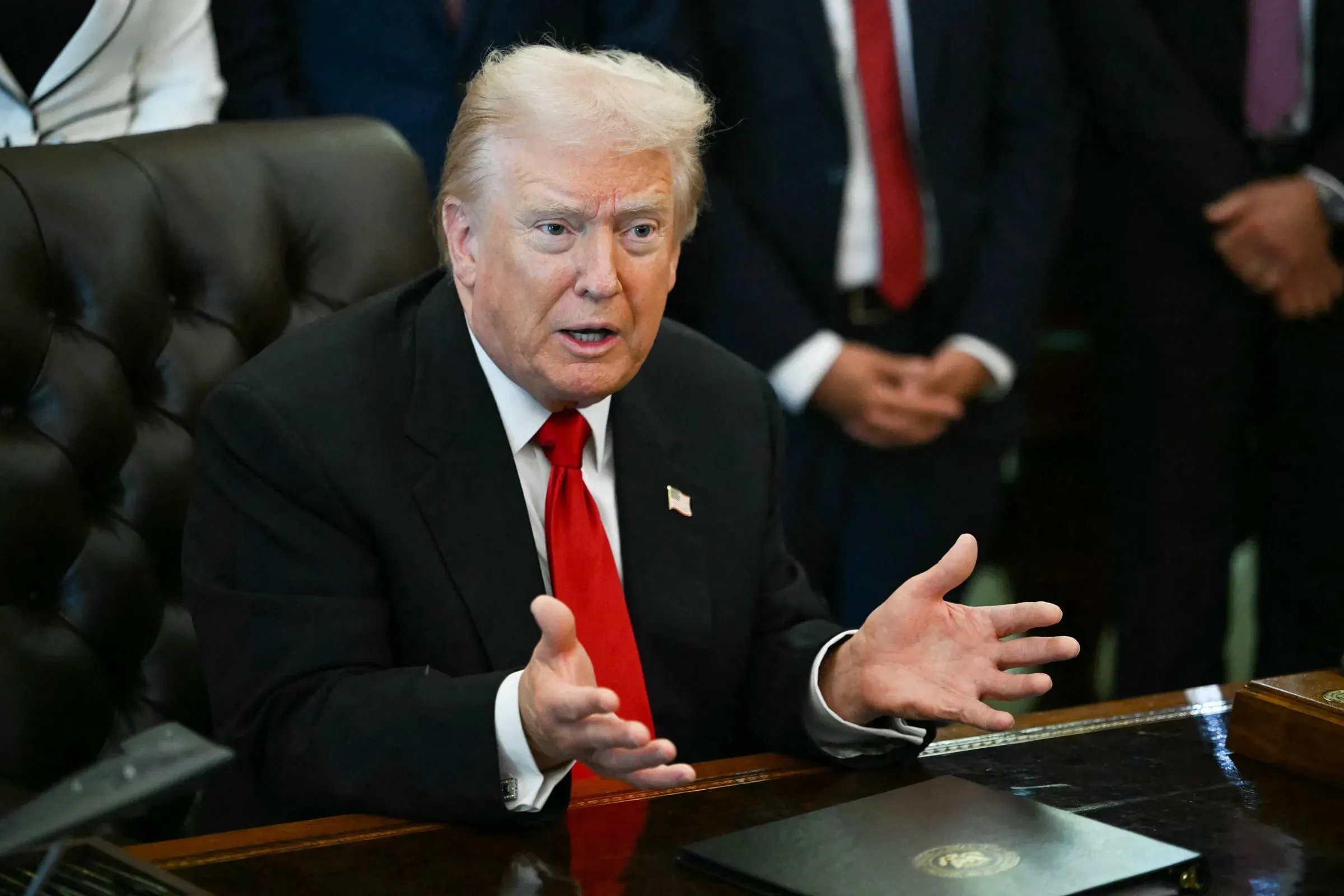 ترامب يتحدث بجدية خلال اجتماع، مع التركيز على قضايا الاقتصاد، وسط مستشارين في الخلفية. تعكس تعابيره إحباطه من ردود فعل الأمريكيين.