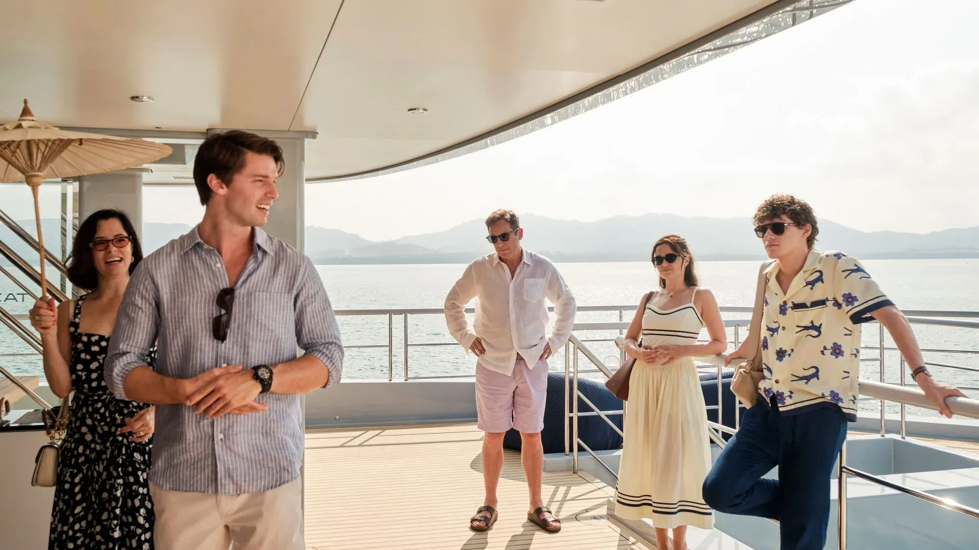 مجموعة من الشخصيات الرئيسية من مسلسل "اللوتس الأبيض" يتفاعلون على متن يخت، مع خلفية بحرية جميلة، حيث تبرز الأجواء الصيفية.