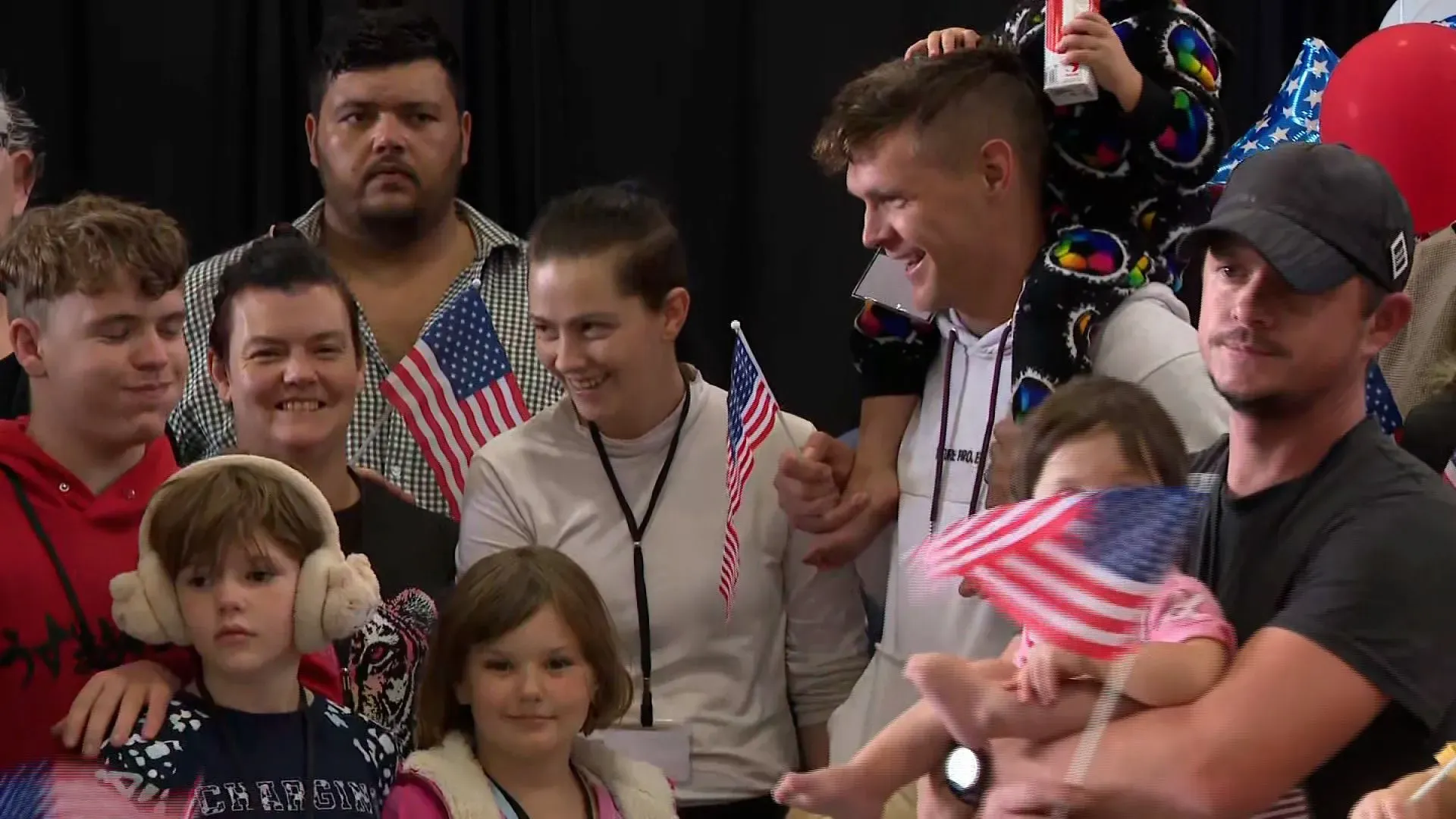 مجموعة من اللاجئين الجنوبيين الأفريقيين البيض تحتفل بوصولهم إلى الولايات المتحدة، حاملي أعلام أمريكية، في مطار واشنطن دالاس.