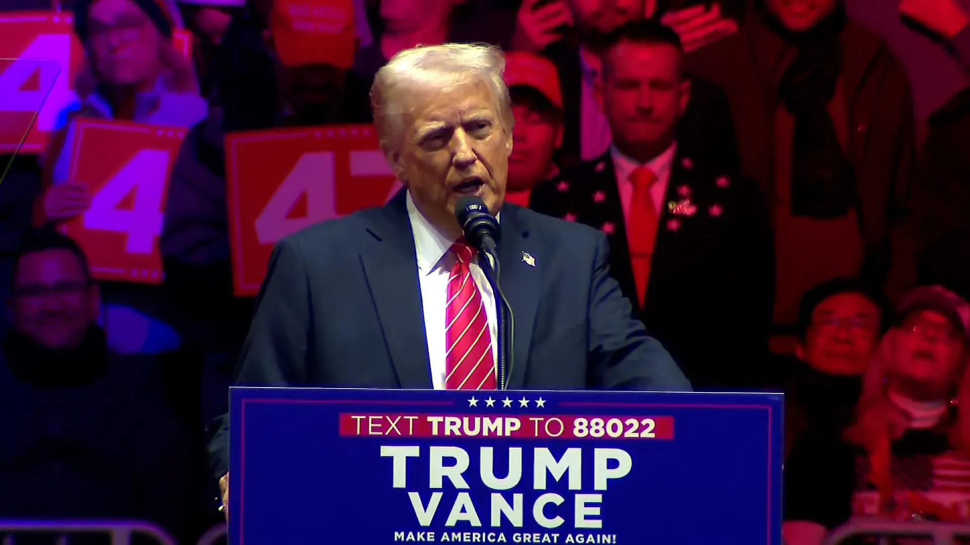 ترامب يتحدث في تجمع انتخابي، محاط بجماهير تحمل لافتات دعماً لحملته، مما يعكس الأجواء الانتخابية في الولايات المتحدة.