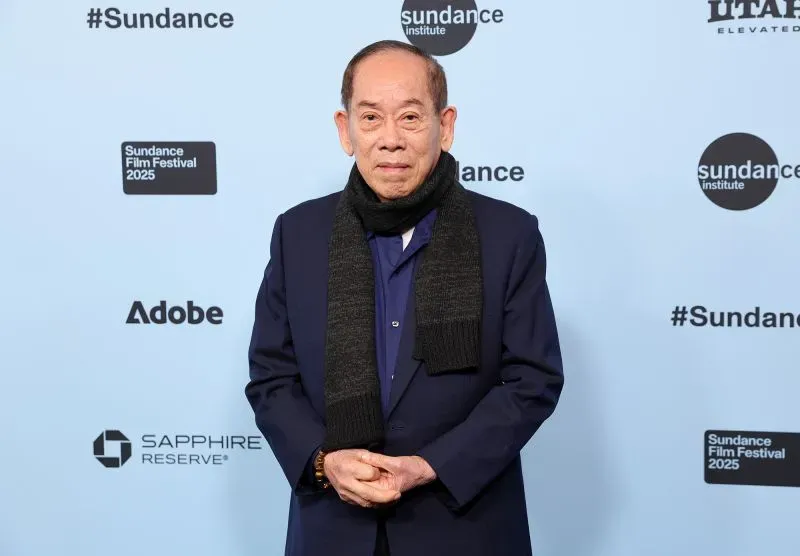 مصور معروف يقف في مهرجان صندانس السينمائي 2025، مرتديًا سترة وقبعة، وسط خلفية تحمل شعارات الحدث.