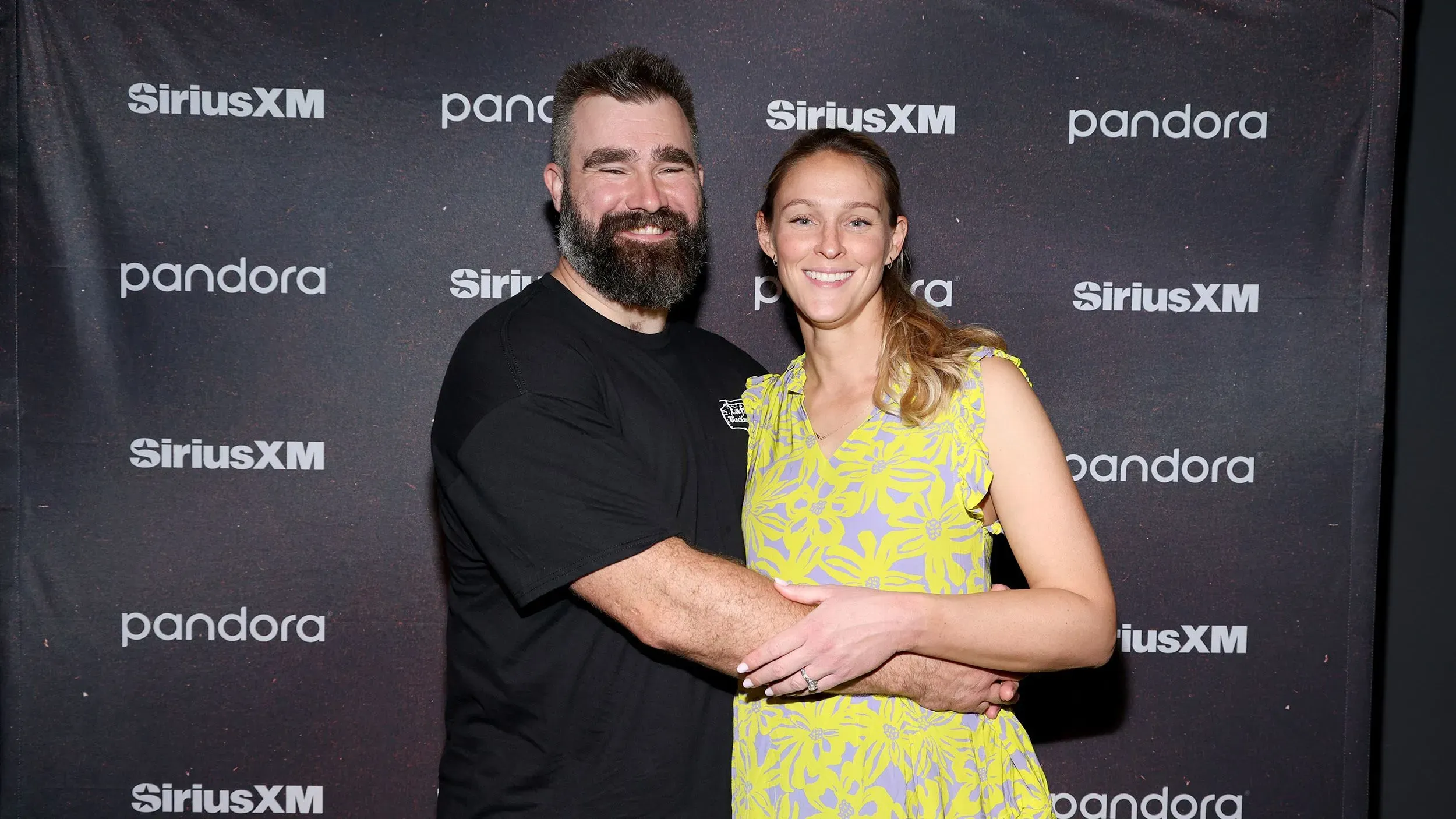 جيسون وكايلي كيلسي يحتفلان بوصول ابنتهما الرابعة، فينلي. يظهر الزوجان مبتسمين في حدث، مع خلفية تحمل شعار "SiriusXM".