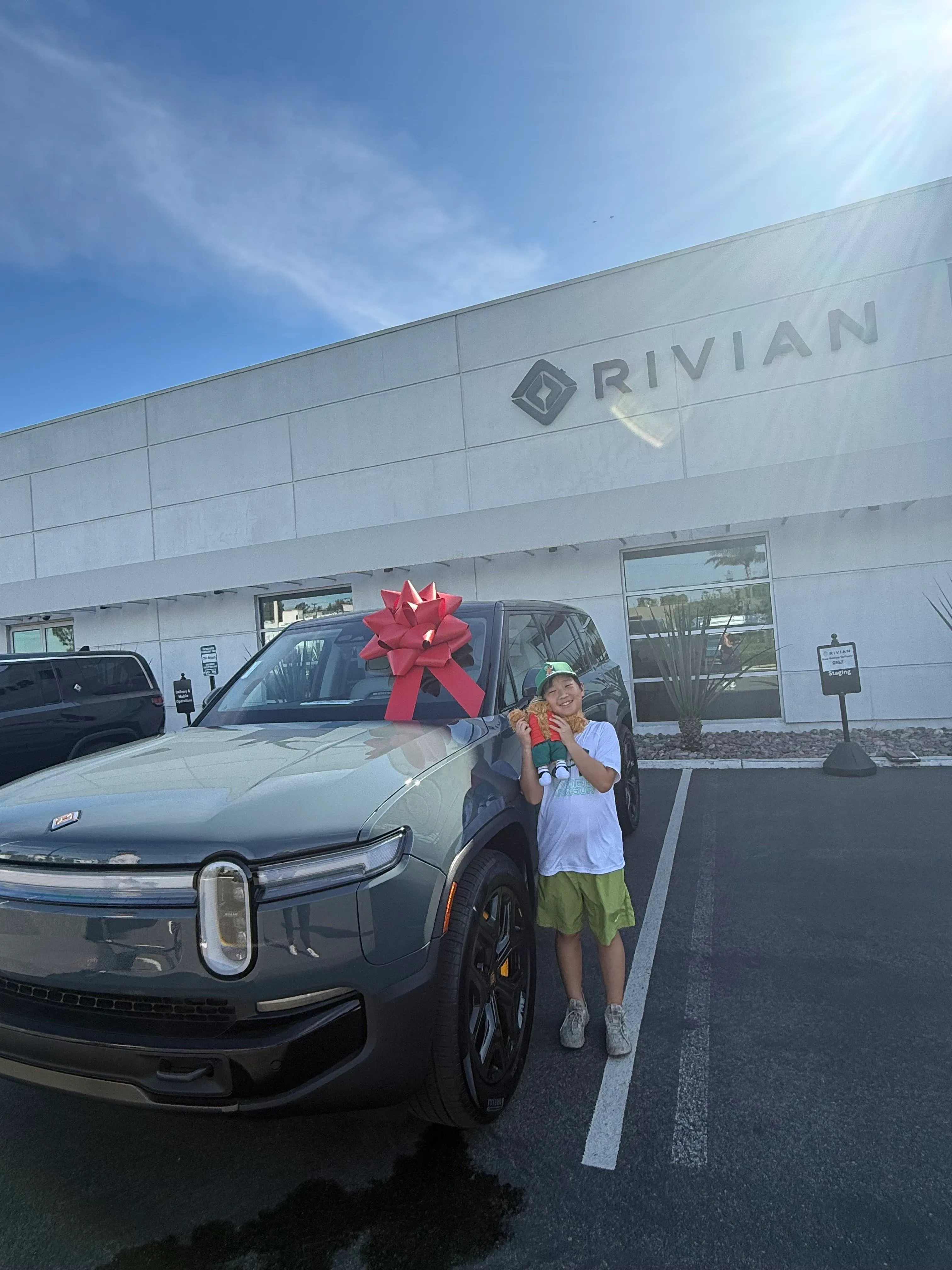 طفل يقف بجانب سيارة كهربائية من نوع Rivian R1، مزينة بشريط أحمر، أمام صالة عرض في جنوب كاليفورنيا.