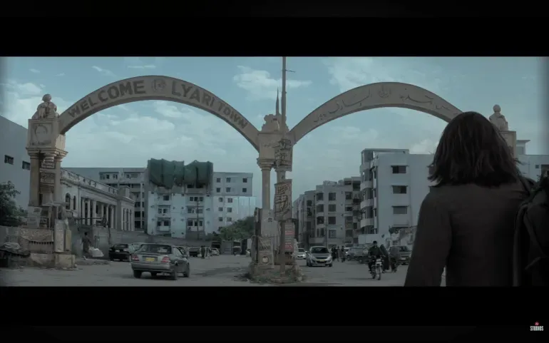 مدخل حي لياري في كراتشي، يظهر لافتة ترحيب، مع خلفية لأبنية سكنية، يعكس أجواء الفيلم البوليوودي "دوراندهار" حول التوترات الهندية-الباكستانية.