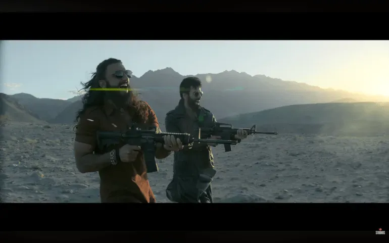 مشهد من فيلم "دوراندهار" يظهر شخصين مسلحين في منطقة جبلية، يعكسان أجواء التوترات بين الهند وباكستان.