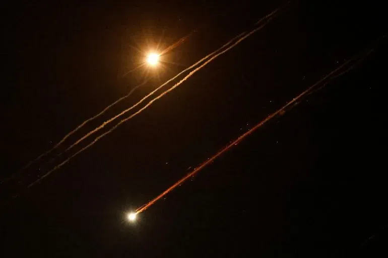 صواريخ مضيئة تنطلق في السماء ليلاً، مع آثار ضوئية تمتد خلفها، مما يعكس تصعيد العنف في الصراع الإسرائيلي الفلسطيني.