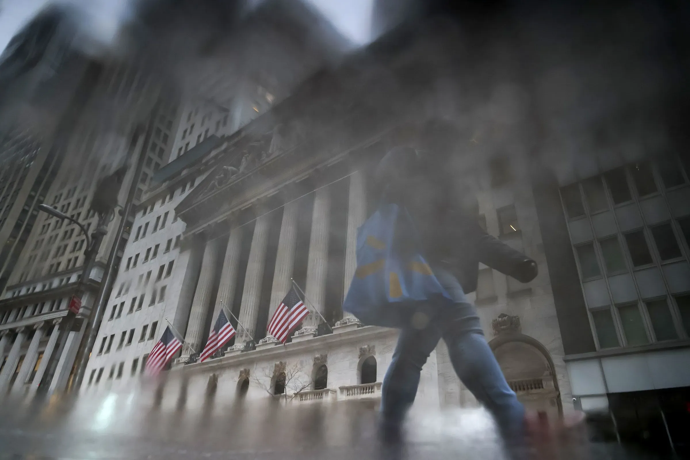 واجهة مبنى البورصة الأمريكية في نيويورك، مع شخص يحمل حقيبة، تعكس القلق الاقتصادي في ظل تباين الثروات.