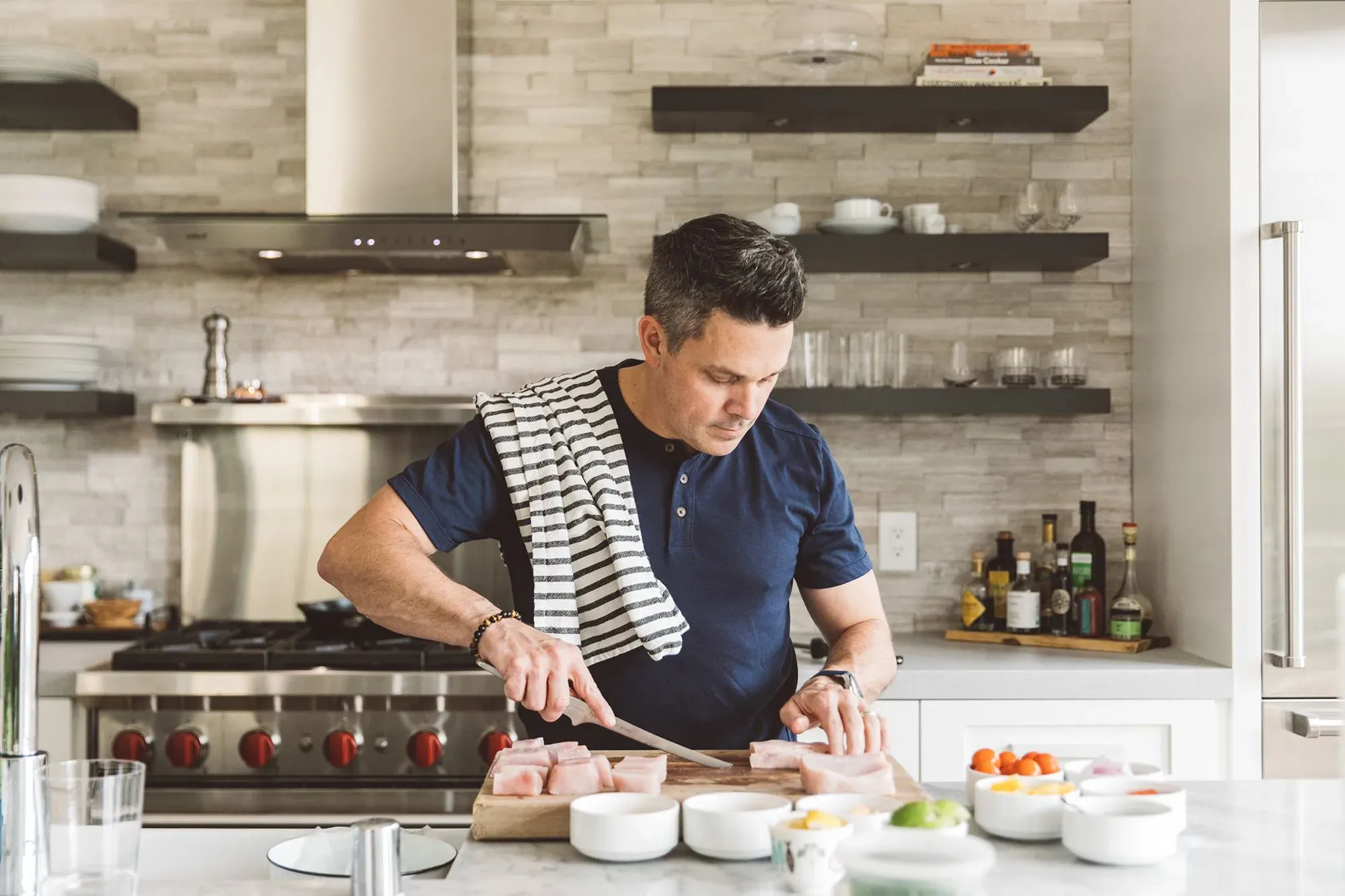 شيف يقف في مطبخ عصري، يقطع الدجاج بينما تحيط به مكونات طهي متنوعة، مستعدًا لإعداد وصفة دجاج وزلابية مستوحاة من جدته.