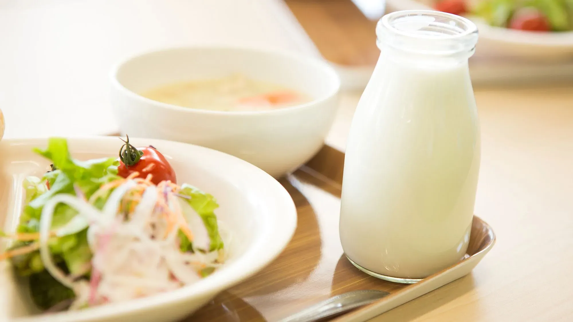 زجاجة حليب كامل الدسم بجانب طبق سلطة وحساء في وجبة مدرسية، تعكس النقاش حول إعادة إدخال الحليب كامل الدسم في المدارس الأمريكية.