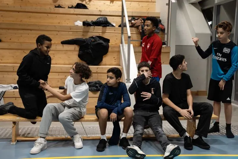 مجموعة من الفتيان تتفاعل في قاعة رياضية خلال "كرة القدم الليلية" في غوتسوندا، حيث يسعى القس روبرت واير هاغ لتوجيههم بعيدًا عن العصابات.