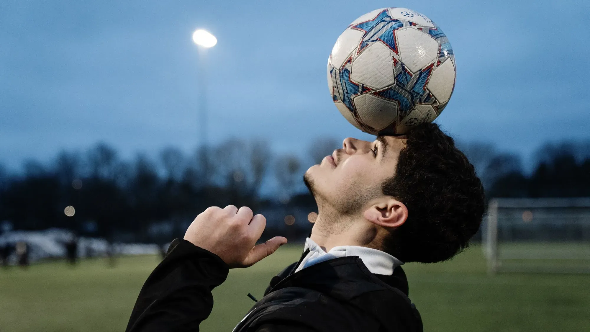 شاب يمارس مهارات كرة القدم بتوازن الكرة على رأسه في ملعب، مما يعكس أهمية الرياضة في حياة الشباب في غوتسوندا.