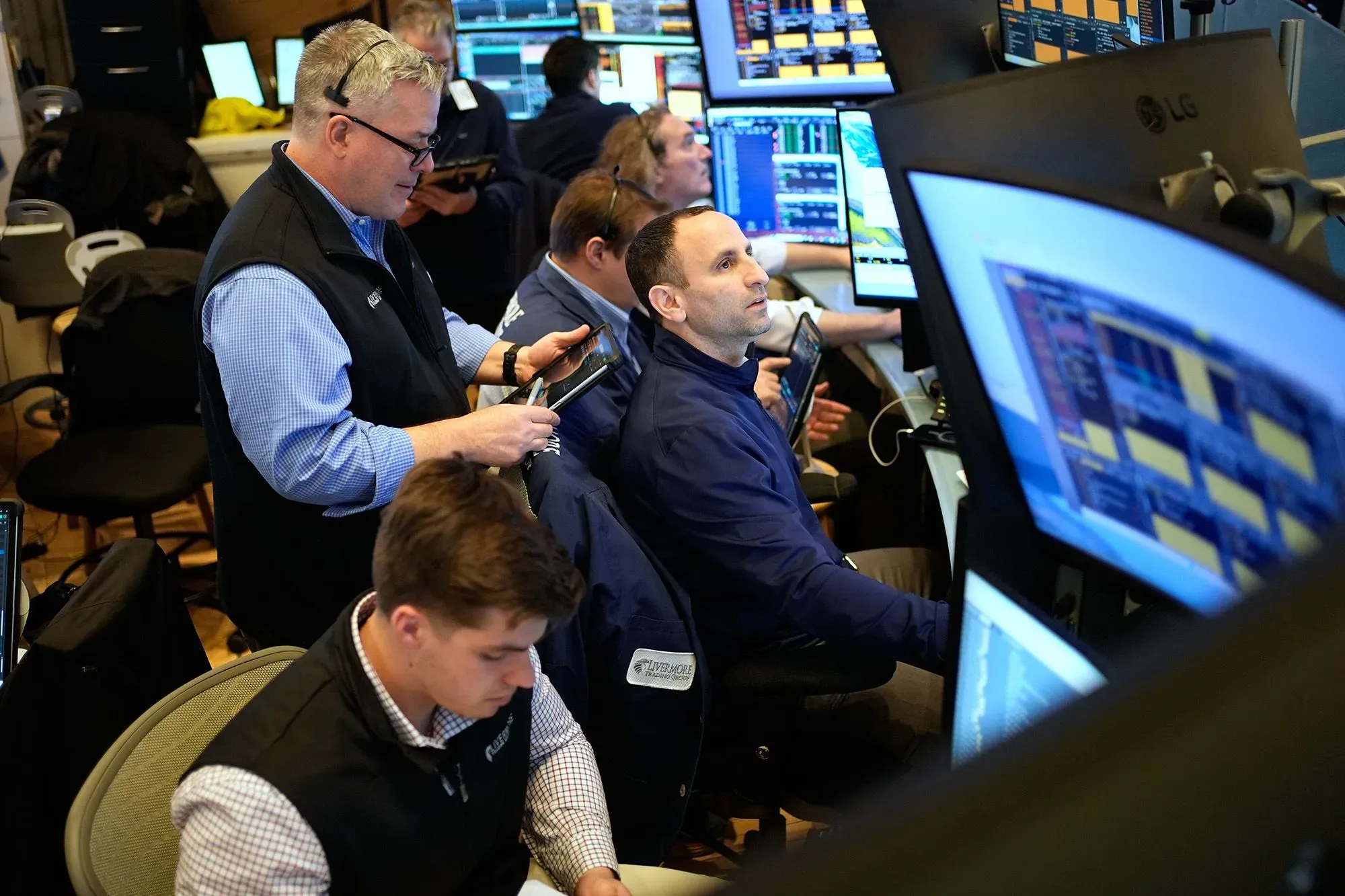 مجموعة من المتداولين في غرفة تداول، يراقبون شاشات متعددة تعرض بيانات السوق، وسط أجواء من التوتر بسبب تقلبات الأسهم.