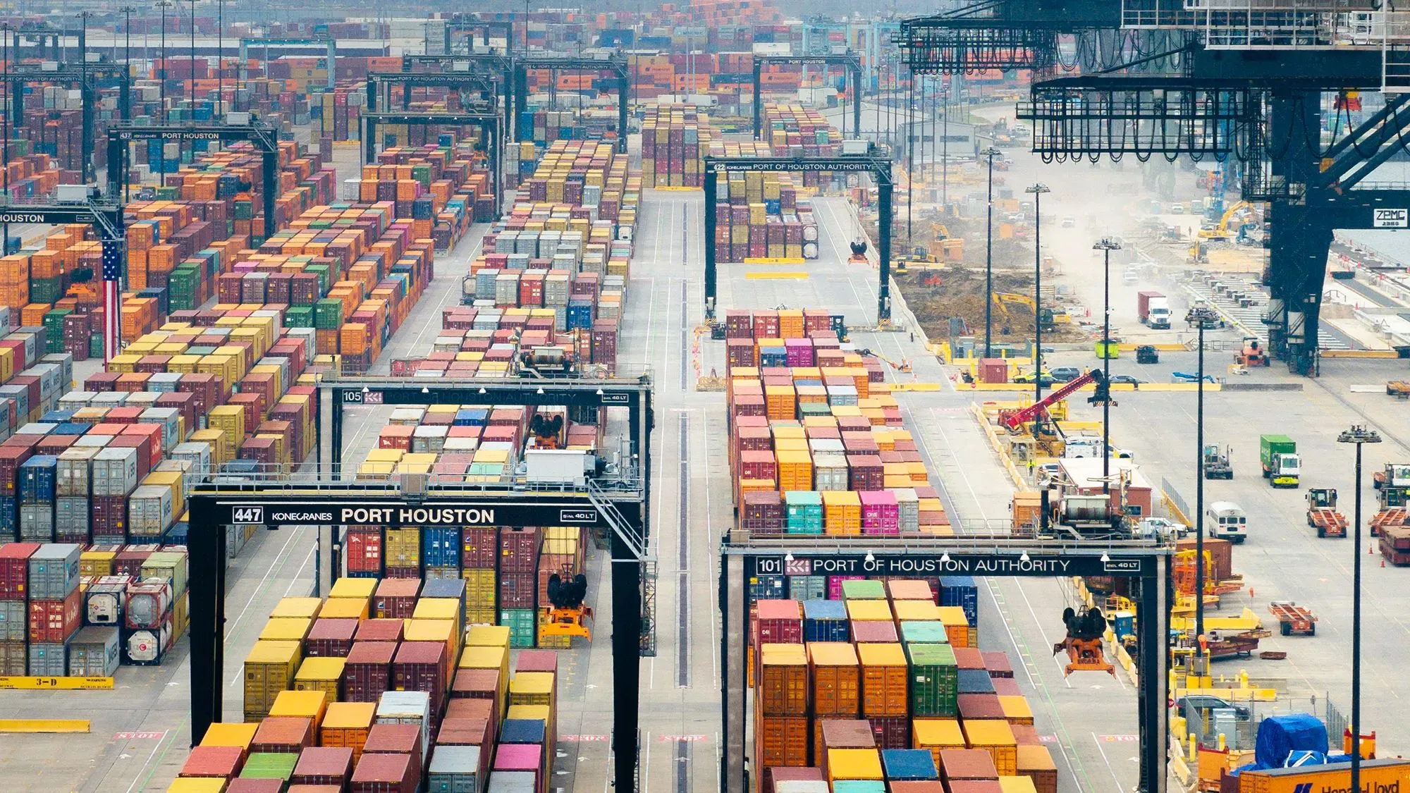 صورة لميناء هيوستن، تُظهر حاويات ملونة مرتبة بشكل منظم، مع رافعات وشاحنات تعمل في الخلفية، تعكس حركة التجارة العالمية.