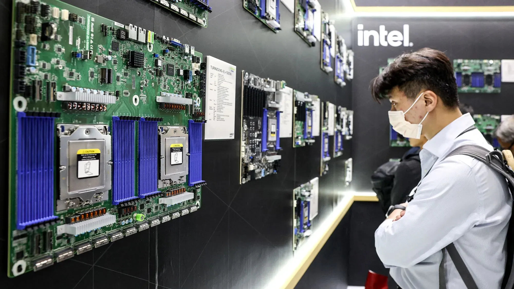 شخص يتأمل لوحات دوائر مطبوعة تحتوي على معالجات وأجزاء إلكترونية، في معرض تكنولوجي يبرز أهمية التغليف المتقدم لأشباه الموصلات.