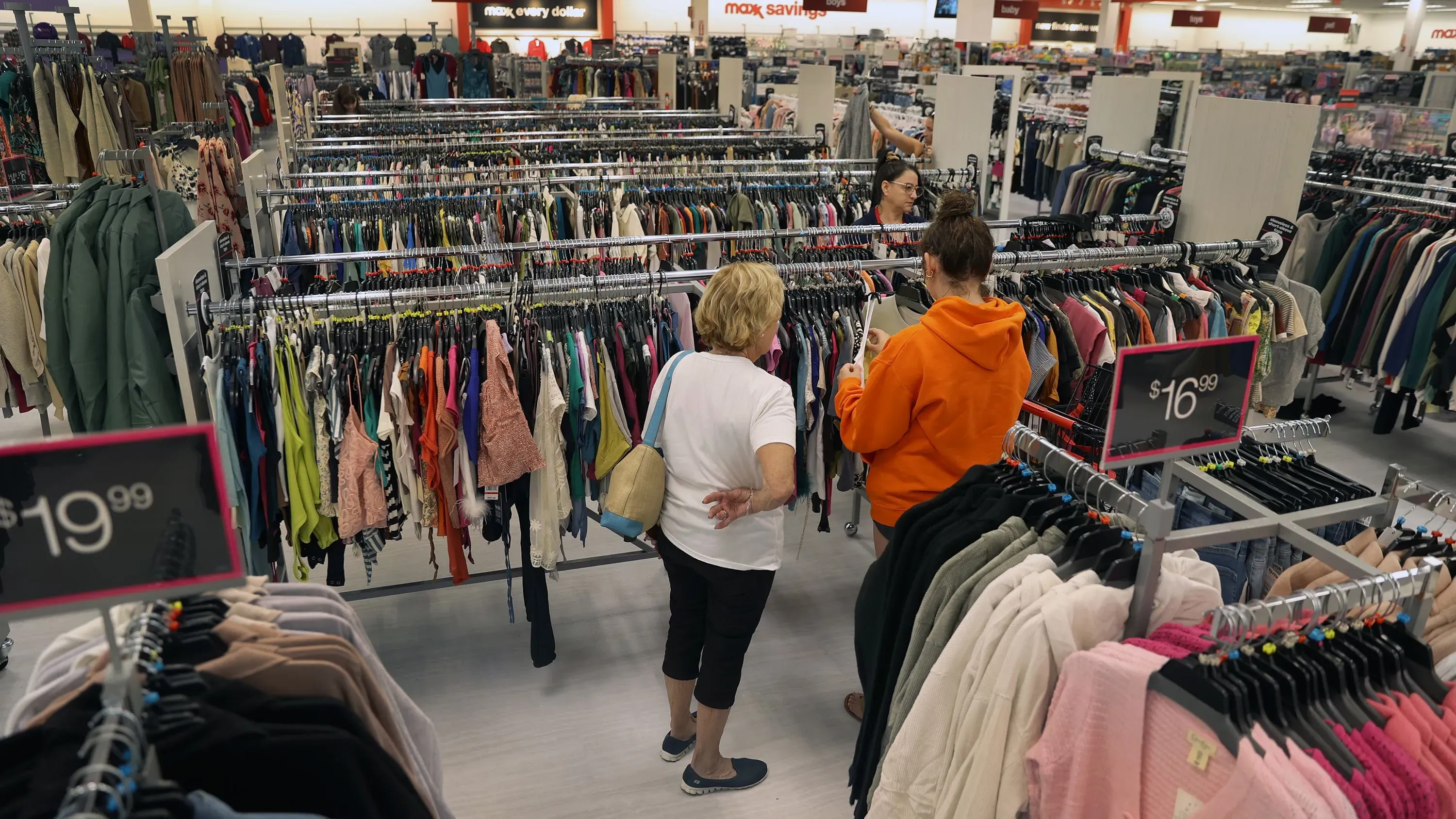 متسوقتان في متجر TJ Maxx تتفقدان الملابس المعروضة، مع وجود لافتات أسعار واضحة تشير إلى التخفيضات.